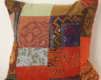 May include: A patchwork pillow cover with a variety of colors and patterns, including red, orange, brown, blue, and green. The cover is made of different fabrics and has a unique, handmade look.