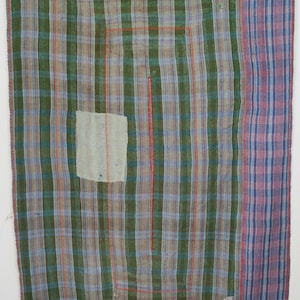 Op de afbeelding: Een patchwork textiel met een ruitpatroon in groen, blauw en bruin. Het textiel heeft een groot blauw vierkant aan de bovenkant en een kleiner blauw vierkant aan de onderkant. Een verticale streep van paars en blauw loopt langs de rechterkant.