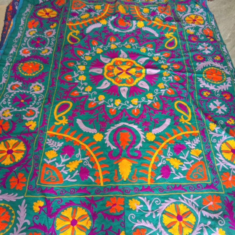 May include: A teal fabric tapestry with intricate embroidery in shades of purple, orange, yellow, and white. The design features floral motifs and paisley patterns.