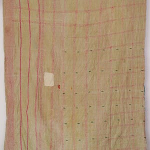 May include: A rectangular textile featuring a light beige base with a grid pattern formed by vertical and horizontal pink stitched lines. The fabric includes small green embroidered accents, two white rectangular patches, and visible running stitch details.