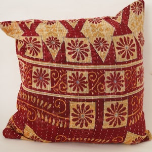 Puede incluir: Una almohada roja y dorada con diseños florales intrincados. La almohada está hecha de una tela suave y acolchada y tiene una forma cuadrada.