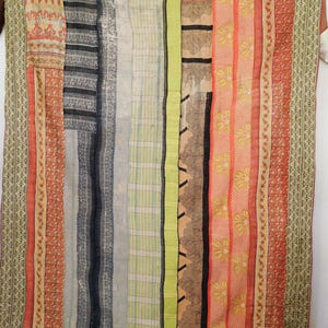 Może przedstawiać: Tekstylny patchwork z wielokolorowymi pionowymi paskami. Wzór obejmuje motywy kwiatowe, geometryczne i w paski w odcieniach czerwieni, pomarańczy, zieleni, niebieskiego i czerni. Tekstylia wykonane są z kilku zszytych ze sobą kawałków materiału.