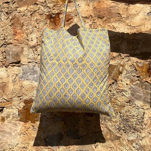 May include: A yellow tote bag with a gray and white geometric pattern. The bag has two handles and is made of fabric.