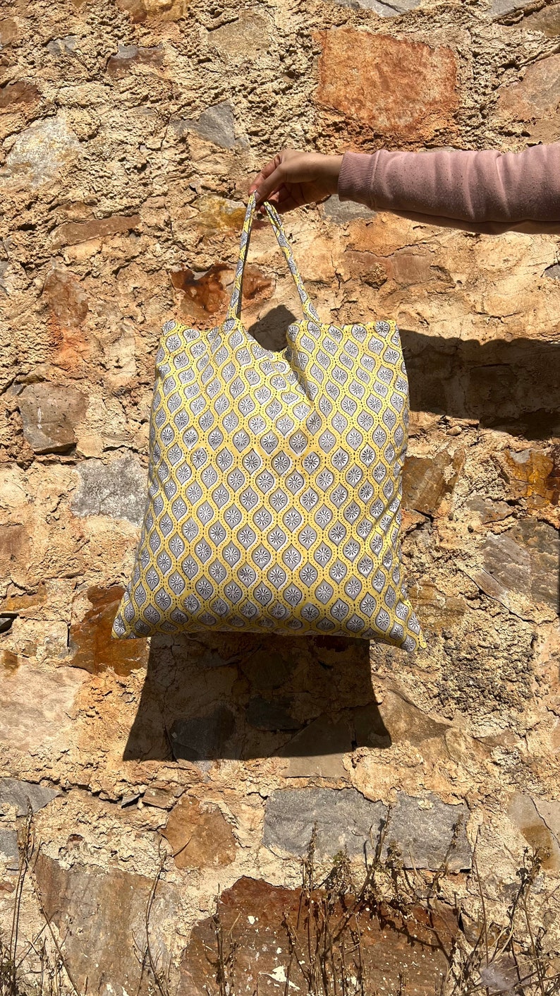 May include: A yellow tote bag with a gray and white geometric pattern. The bag has two handles and is made of fabric.