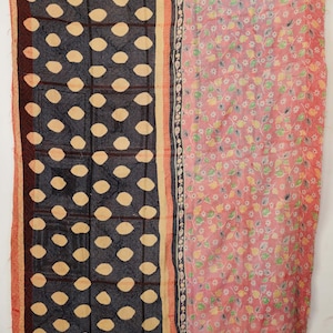 May include: A patchwork quilt with a dark blue pattern of large, light-colored ovals and a pink floral pattern. The quilt has a red and beige border and is likely made of cotton.