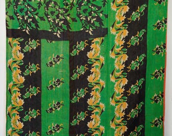 Op de afbeelding: Een rechthoekig textiel met een patchworkontwerp met afwisselende verticale strepen in felgroen en zwart. De stof is versierd met herhalende bloemmotieven in tinten geel, wit en zwart, met zichtbare fijne stiksels over het gehele oppervlak.