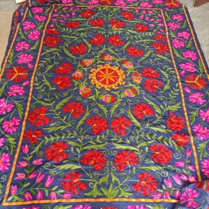 May include: A blue fabric tapestry with intricate embroidery featuring red, pink, and yellow flowers. The design is symmetrical and includes a central circular motif.