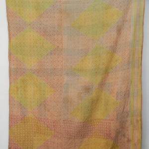May include: A vintage textile with a geometric pattern. The fabric features large diamond shapes in shades of yellow and peach, with a repeating circular pattern in the background. The edges have a striped border in yellow and peach.