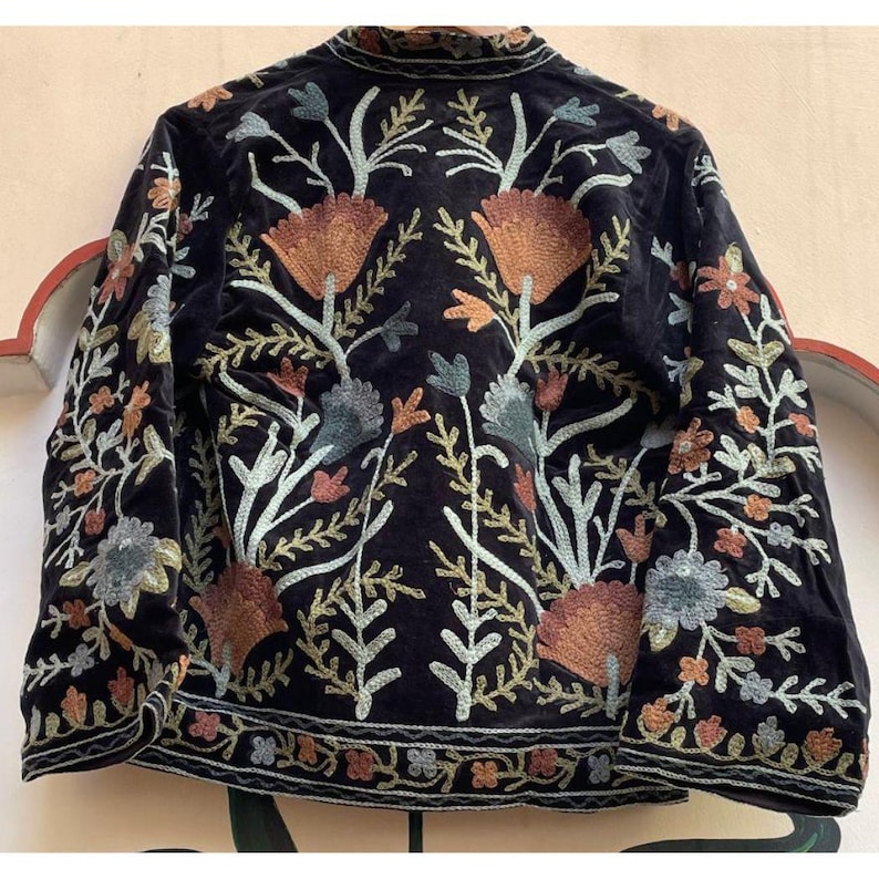 May include: Black velvet jacket with detailed floral embroidery in orange, green, and blue. The jacket has a high collar and embroidered sleeves and hem. A stylish outerwear piece, perfect for adding a touch of elegance.