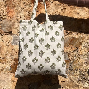 May include: White tote bag with a green floral print. The bag has two handles and is made of a soft, natural fabric.