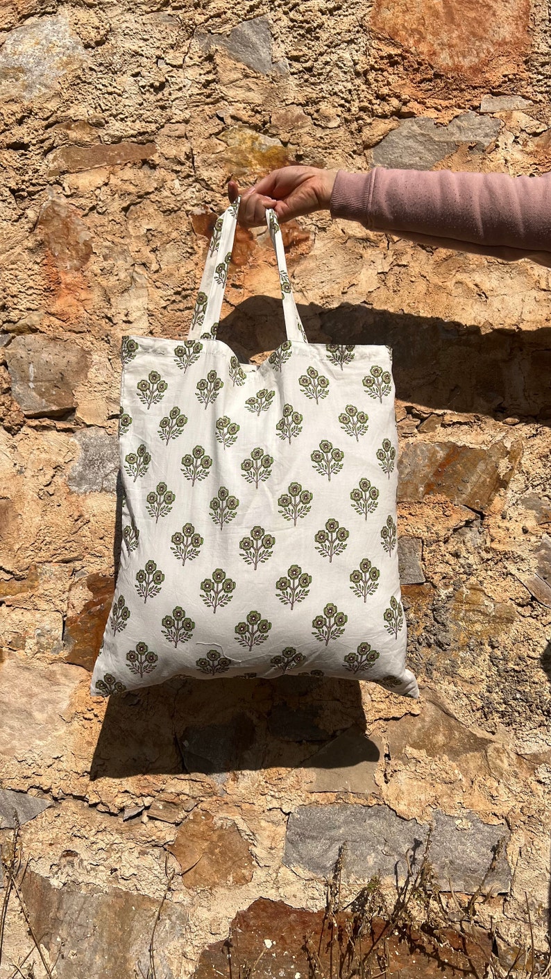 May include: White tote bag with a green floral print. The bag has two handles and is made of a soft, natural fabric.