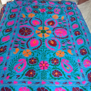 May include: A blue fabric square with a colorful floral embroidery pattern. The design features pink, orange, green, and maroon flowers with intricate details.