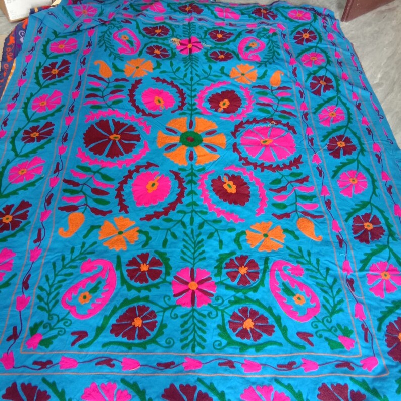 May include: A blue fabric square with a colorful floral embroidery pattern. The design features pink, orange, green, and maroon flowers with intricate details.