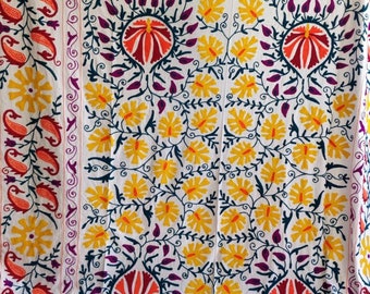 May include: White cotton fabric with a colorful floral embroidery design. The embroidery features yellow, red, orange, purple, and blue flowers and leaves. The fabric has a square shape and is perfect for a tablecloth, wall hanging, or throw.