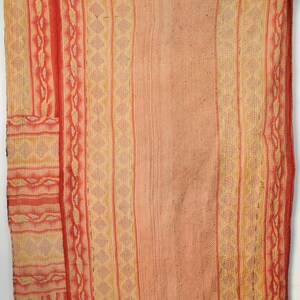 May include: A hand-stitched textile with a peach-coloured background and vertical stripes in shades of red, orange, and yellow. The stripes feature geometric patterns and decorative stitching. The textile appears to be a blanket or throw.