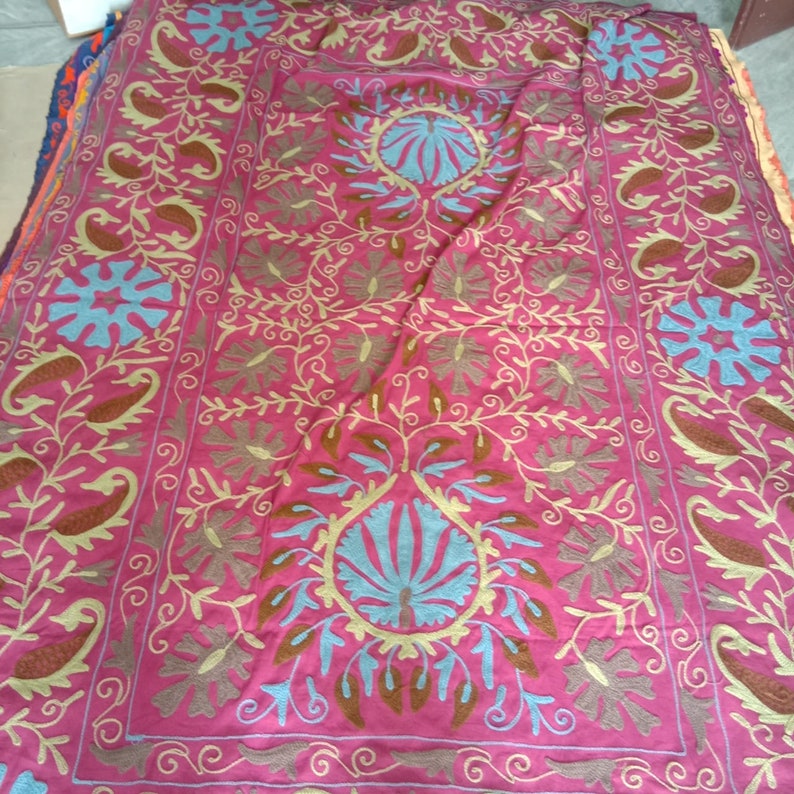 May include: A pink fabric throw blanket with intricate embroidery in brown, blue, and yellow. The design features floral patterns and paisley motifs.