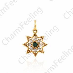 Op de afbeelding: Een gouden hanger in de vorm van een ster met een groene edelsteen in het midden en heldere strasssteentjes rond de randen.