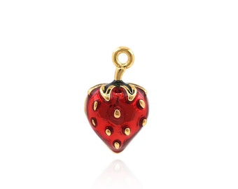 Puede incluir: Un charm de color dorado en forma de fresa roja con contornos negros y detalles dorados. La fresa tiene un tallo y hojas verdes.