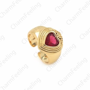 May include: A gold ring with a red heart-shaped stone. The ring is designed to fit on the thumb.