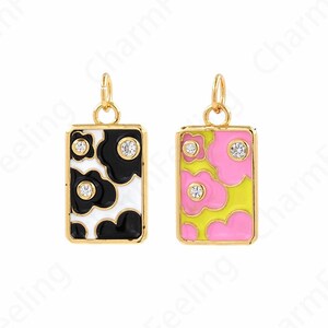 May include: Two gold charm pendants with enamel floral designs. One pendant is black and white with clear rhinestones, the other is pink and yellow with clear rhinestones.