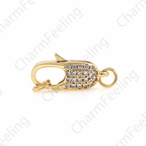 May include: Gold-toned clasp with a clear crystal design. The clasp is a lobster claw style with a small loop on the side.