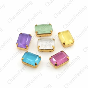 May include: Assortment of six rectangular glass rhinestones with gold settings. The rhinestones are in various colors, including light blue, light green, clear, light pink, yellow, and purple.