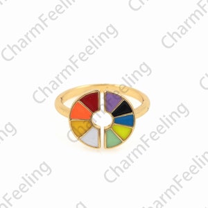 May include: A gold ring with a colorful enamel design. The design is a circle with a hole in the center and is divided into 10 sections, each a different color. The colors are red, orange, yellow, green, blue, purple, pink, white, black, and light blue.