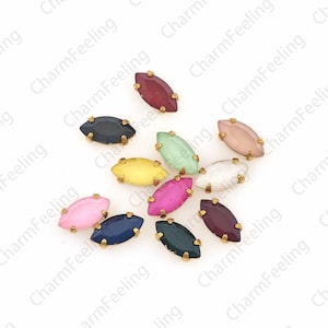 May include: Assortment of ten small, oval-shaped, glass rhinestones with gold settings. The rhinestones are in various colors, including red, pink, green, blue, yellow, and purple.