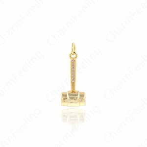 May include: A gold-toned charm in the shape of a gavel with a row of clear cubic zirconia stones on the handle.