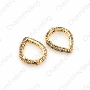 May include: Two gold-tone teardrop-shaped clasps with clear crystal accents. The clasps are open and ready to be attached to a jewelry piece.