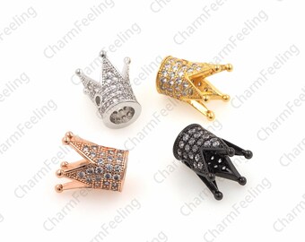 May include: Four small crown-shaped charms in silver, gold, rose gold, and black. Each charm is encrusted with small, clear gemstones. The crowns have a cylindrical base and are designed for jewelry making or crafting.