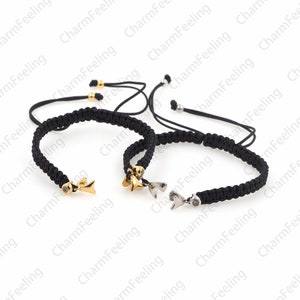 Puede incluir: Dos pulseras trenzadas negras con cierres ajustables. Una pulsera tiene un dije de oro en forma de pez con una peque&ntilde;a piedra transparente. La otra pulsera tiene un dije de plata en forma de coraz&oacute;n con una peque&ntilde;a piedra transparente.
