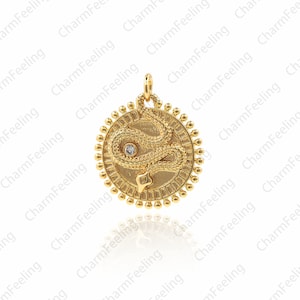 以下が含まれることがあります： 目は透明な小さな石で飾られた蛇のデザインの金色のペンダント。蛇はビーズの縁のある円盤に巻き付けられている。