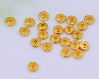 May include: A collection of small, gold-colored watch crowns scattered on a white surface. Each crown has a circular design with a ridged edge and a central hole. The crowns are likely for watch repair or jewelry making.