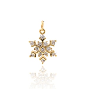 Op de afbeelding: Een gouden sneeuwvlok hanger met heldere kristallen. De hanger is op een witte achtergrond.