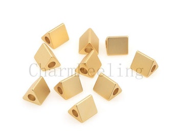 May include: Ten gold-colored triangle-shaped beads with a hole in the center of each bead. The beads are scattered on a white surface.