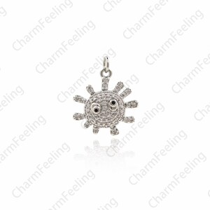 May include: A silver charm in the shape of a sun with a face. The sun has small, round, white stones for eyes and a black center. The sun is surrounded by a ring of small, white stones.