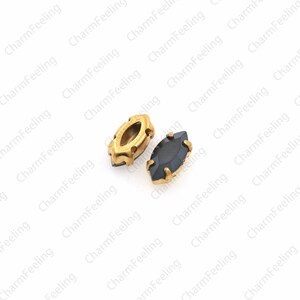 May include: Two small, gold-rimmed, oval-shaped rhinestones. One is clear and the other is black.