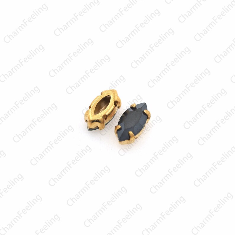 May include: Two small, gold-rimmed, oval-shaped rhinestones. One is clear and the other is black.