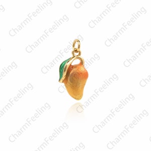 Puede incluir: Un charm de oro en forma de mango con una hoja verde. El mango es naranja y amarillo con un acabado brillante.