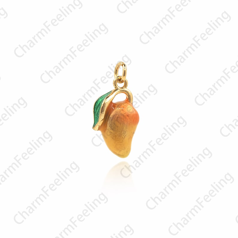 Puede incluir: Un charm de oro en forma de mango con una hoja verde. El mango es naranja y amarillo con un acabado brillante.