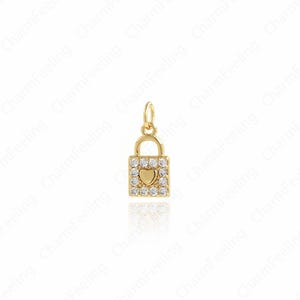 May include: A gold-coloured padlock charm featuring a heart-shaped centre and clear crystals. The charm has a small loop at the top for attachment. The charm is likely made of metal and suitable for jewellery.
