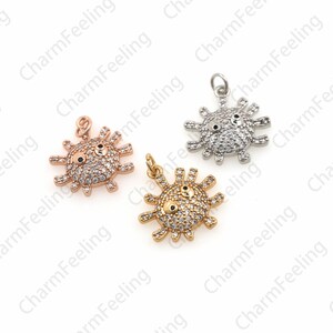May include: Three charm pendants in the shape of a cartoon sun with a face. The sun is made of metal and has clear rhinestones for eyes. The pendants are in gold, silver, and rose gold.