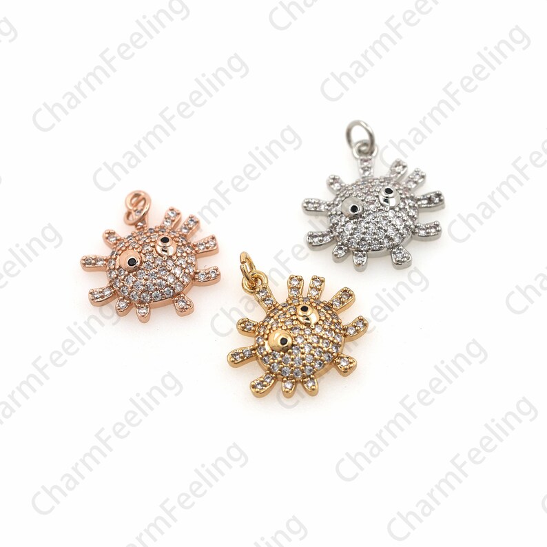 May include: Three charm pendants in the shape of a cartoon sun with a face. The sun is made of metal and has clear rhinestones for eyes. The pendants are in gold, silver, and rose gold.