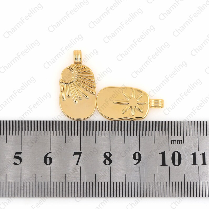 May include: Two gold-tone metal charms, one with a sun design and the other with a star design, are measured on a ruler. The charms are approximately 1 inch in length.