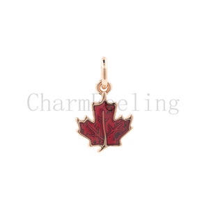 May include: A gold-toned charm in the shape of a red maple leaf. The leaf has a detailed design and is a popular symbol of Canada.