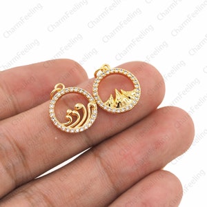 May include: Two gold-toned charms with clear crystal accents. One charm features a wave design and the other charm features a mountain design.