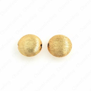May include: Two gold-coloured, round beads with a textured surface. Each bead has a small hole for stringing. The beads are made of metal and are suitable for jewellery making or other craft projects.