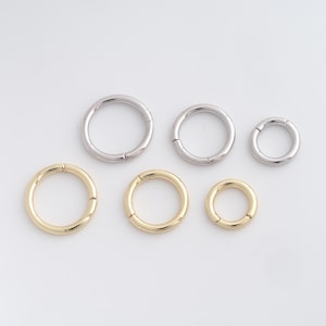Puede incluir: Seis pendientes de aro metálicos de diferentes tamaños. Tres son plateados y tres dorados. Los pendientes se muestran sobre un fondo blanco, resaltando su diseño circular y cierres.