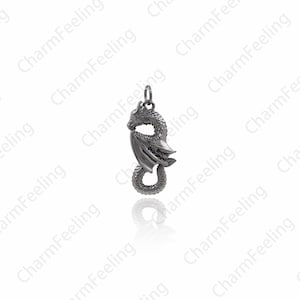 May include: A silver dragon charm pendant with detailed wings and a curled tail. The dragon is facing to the left and has a textured surface.